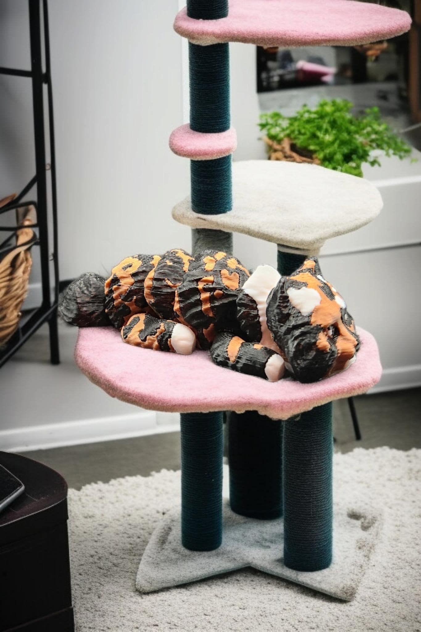 3D printed articulated cat figurine lying on a pink platform of a multi-level cat tree