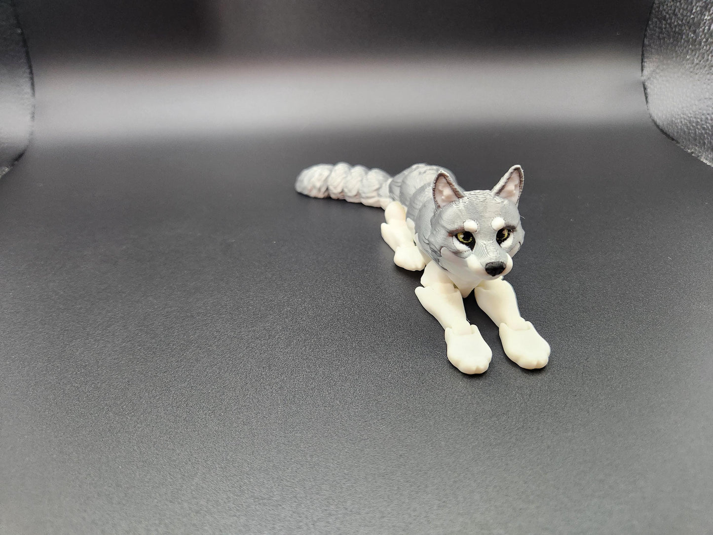 3D printed realistic wolf figurine in gray and white colors lying down on black surface