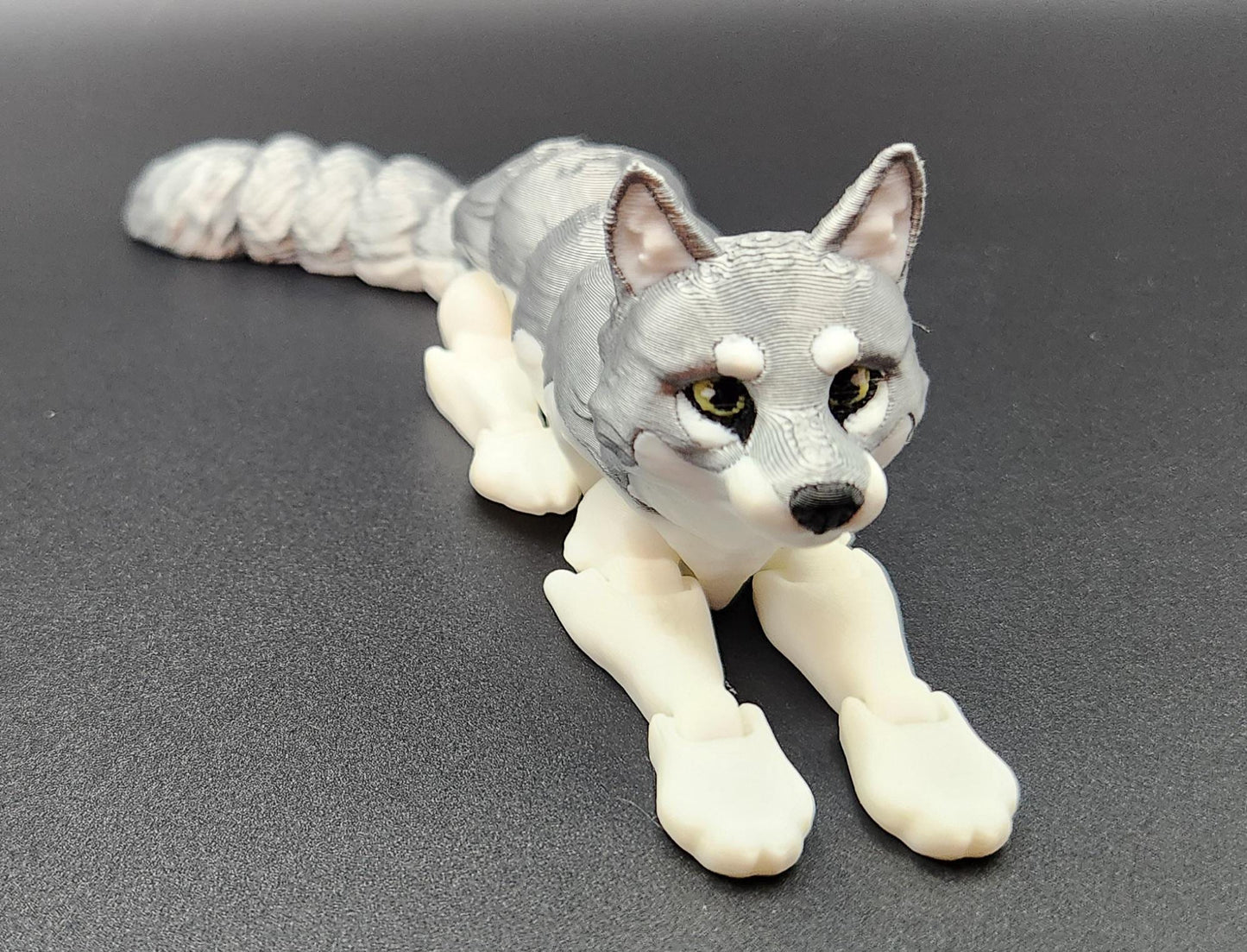 3D printed realistic wolf figurine in gray and white lying down on black surface