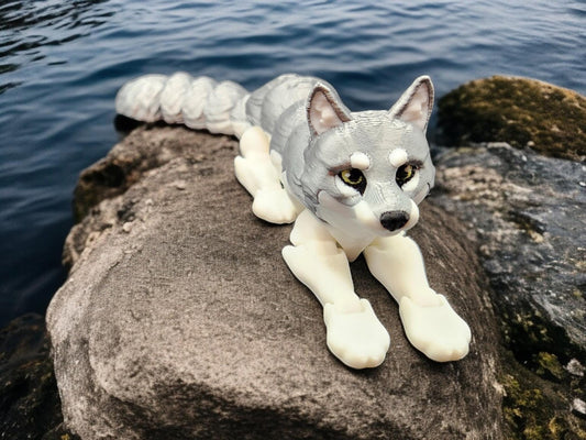 3D printed realistic wolf figurine with detailed features resting on a rock near water