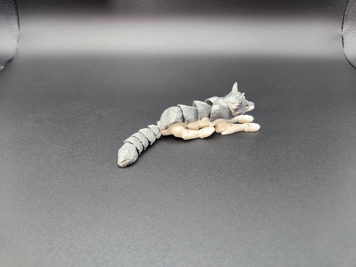 3D printed realistic wolf figurine in gray and beige lying down on black background