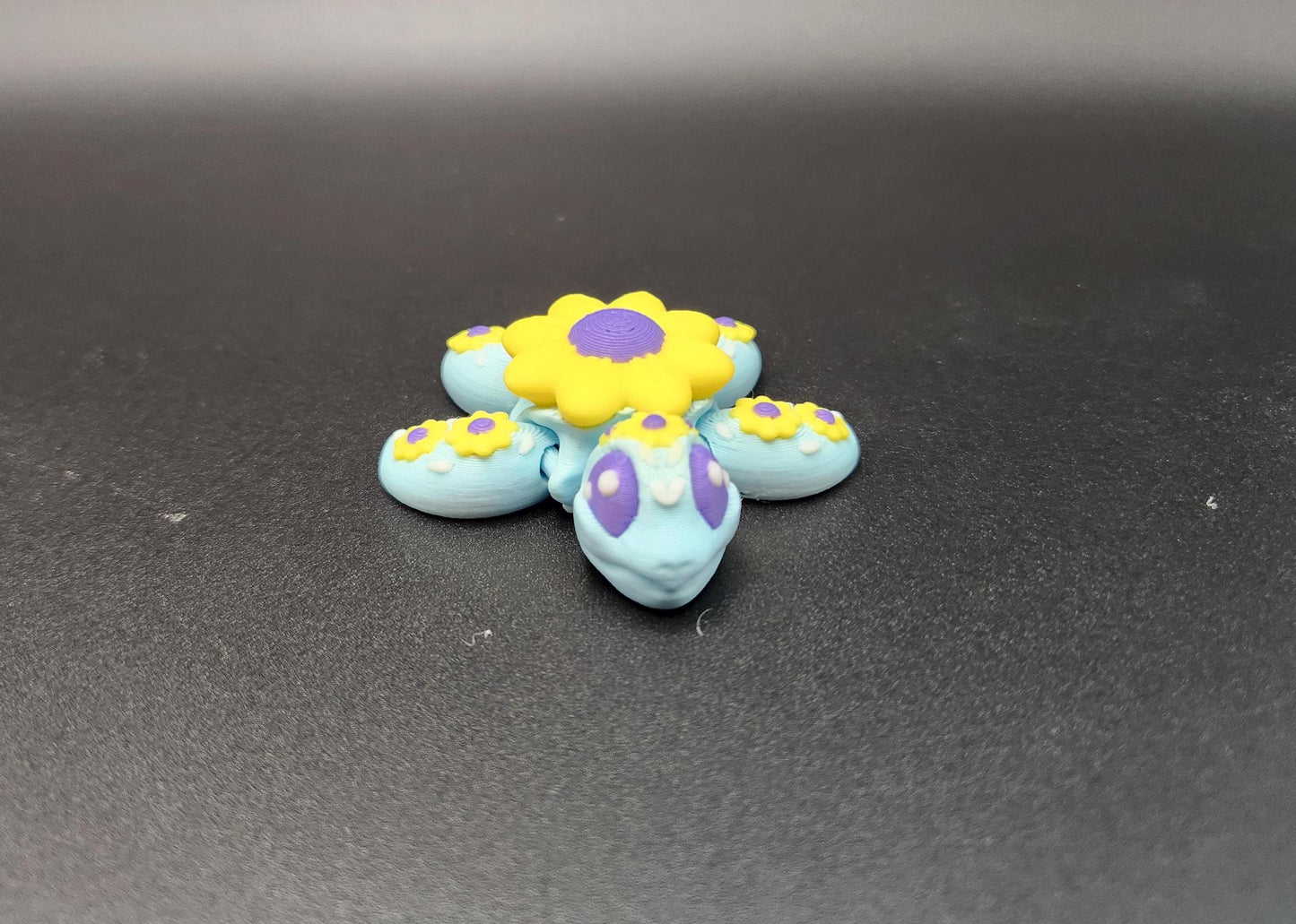 3D printed sunflower turtle with blue body and yellow sunflower patterns on black background