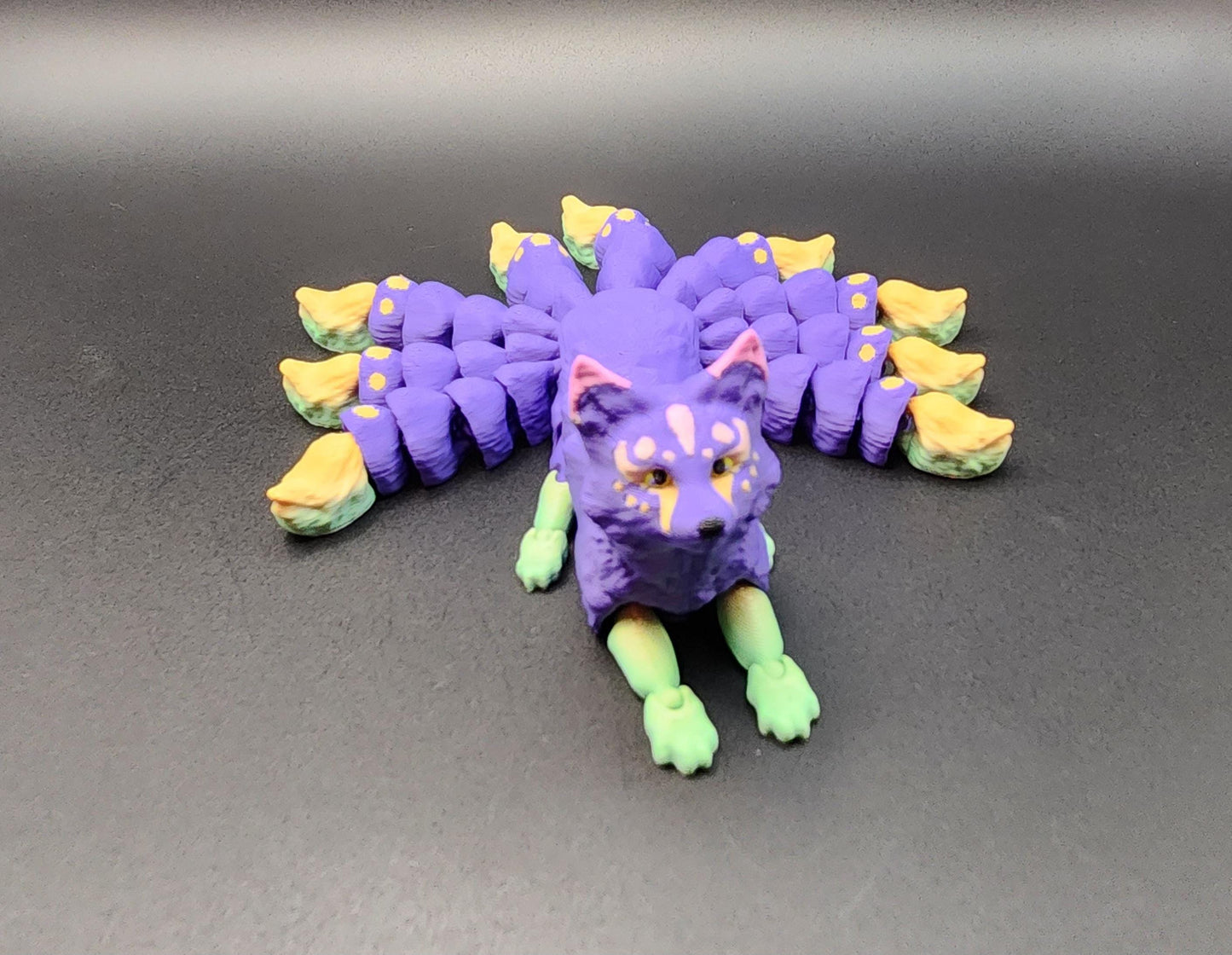 Colorful purple and yellow Japanese kitsune figurine 9-tailed fox mythical creature on black background