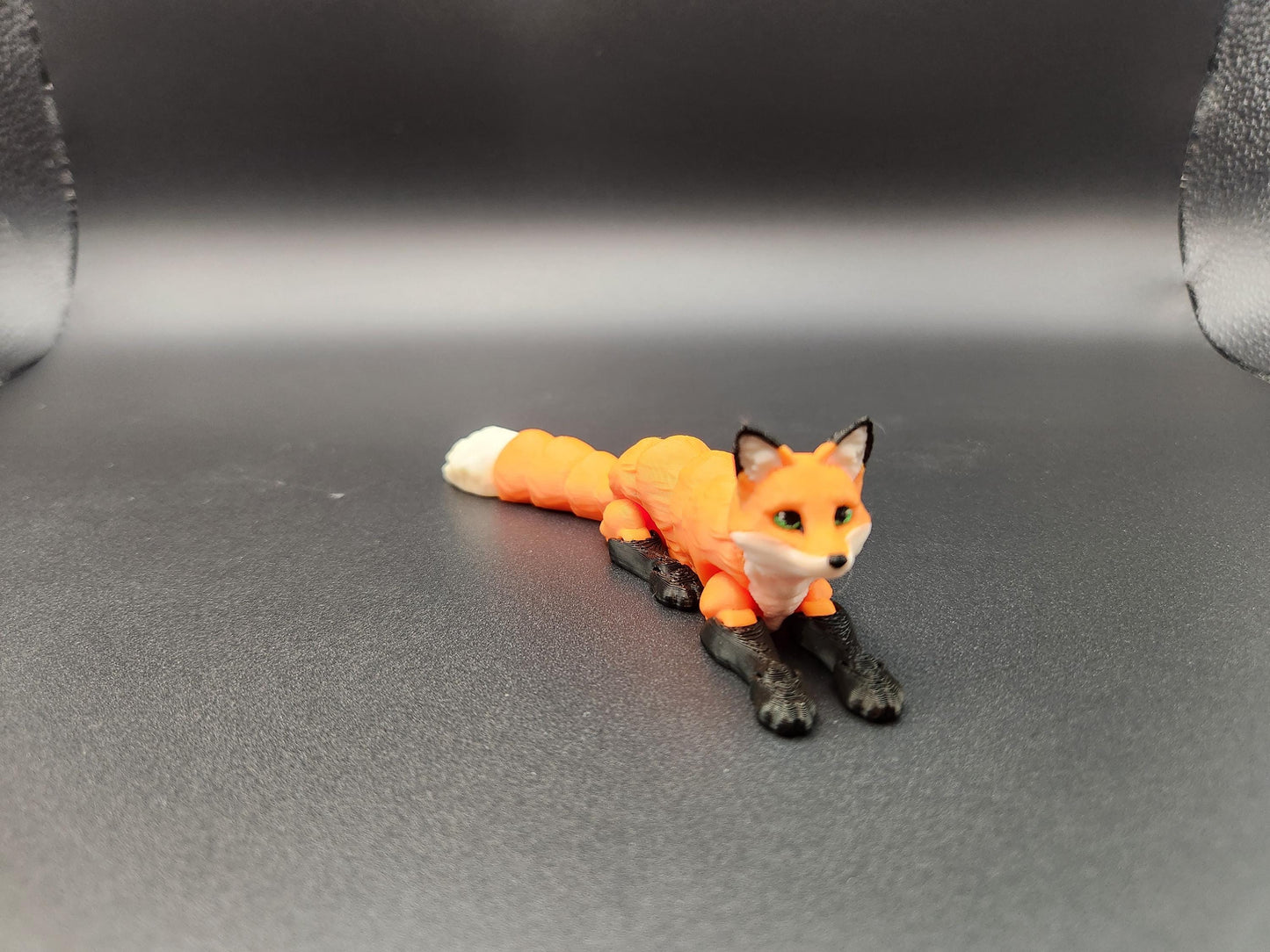 Realistic 3D printed Articulated fox figurine in orange and black lying down on a black surface