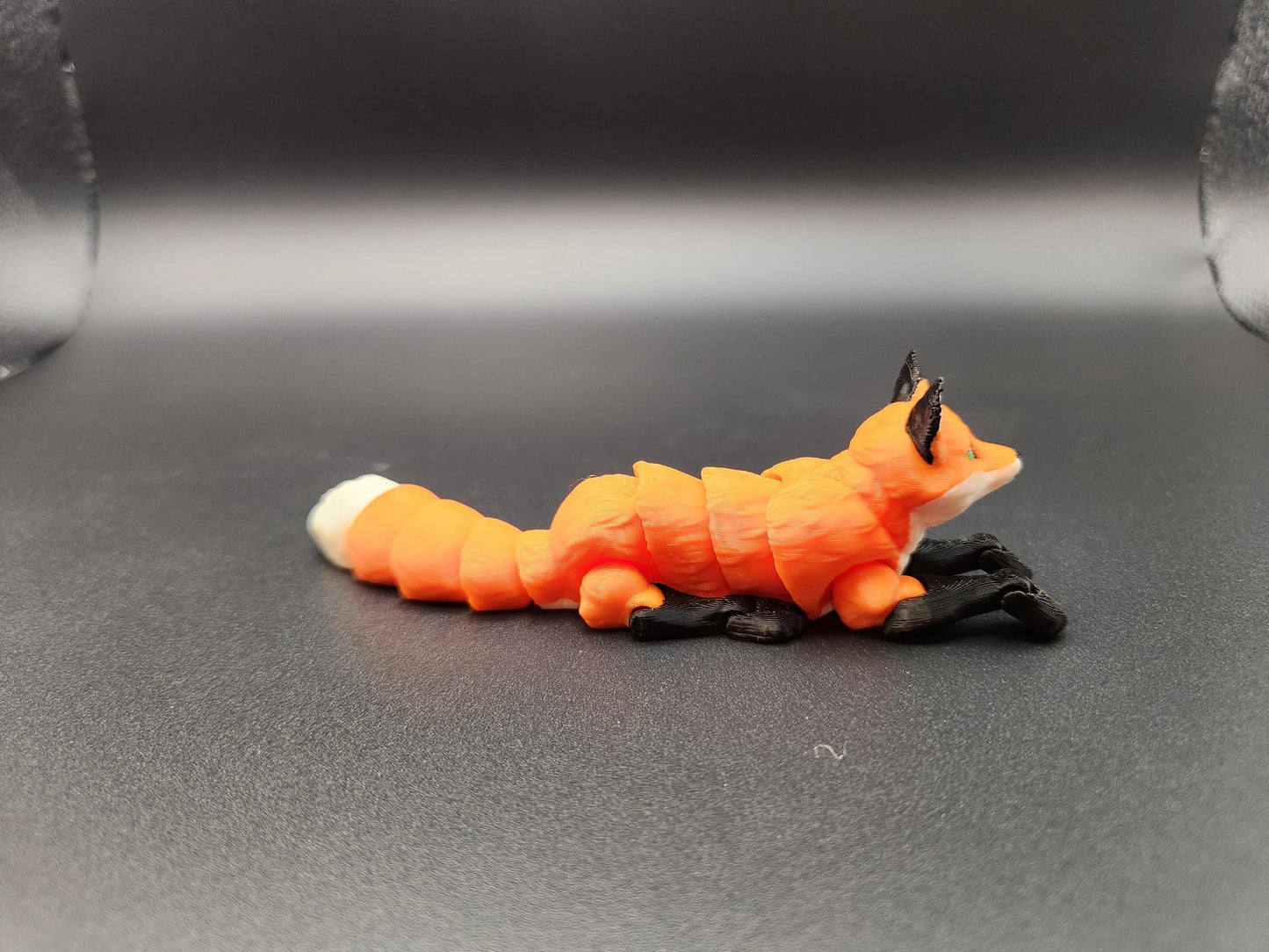 Realistic 3D printed Articulated fox figurine in orange and black resting on a black surface