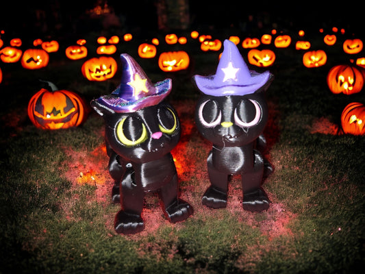 3D printed articulated cat figurine wearing purple and blue witch hats surrounded by glowing jack-o-lanterns