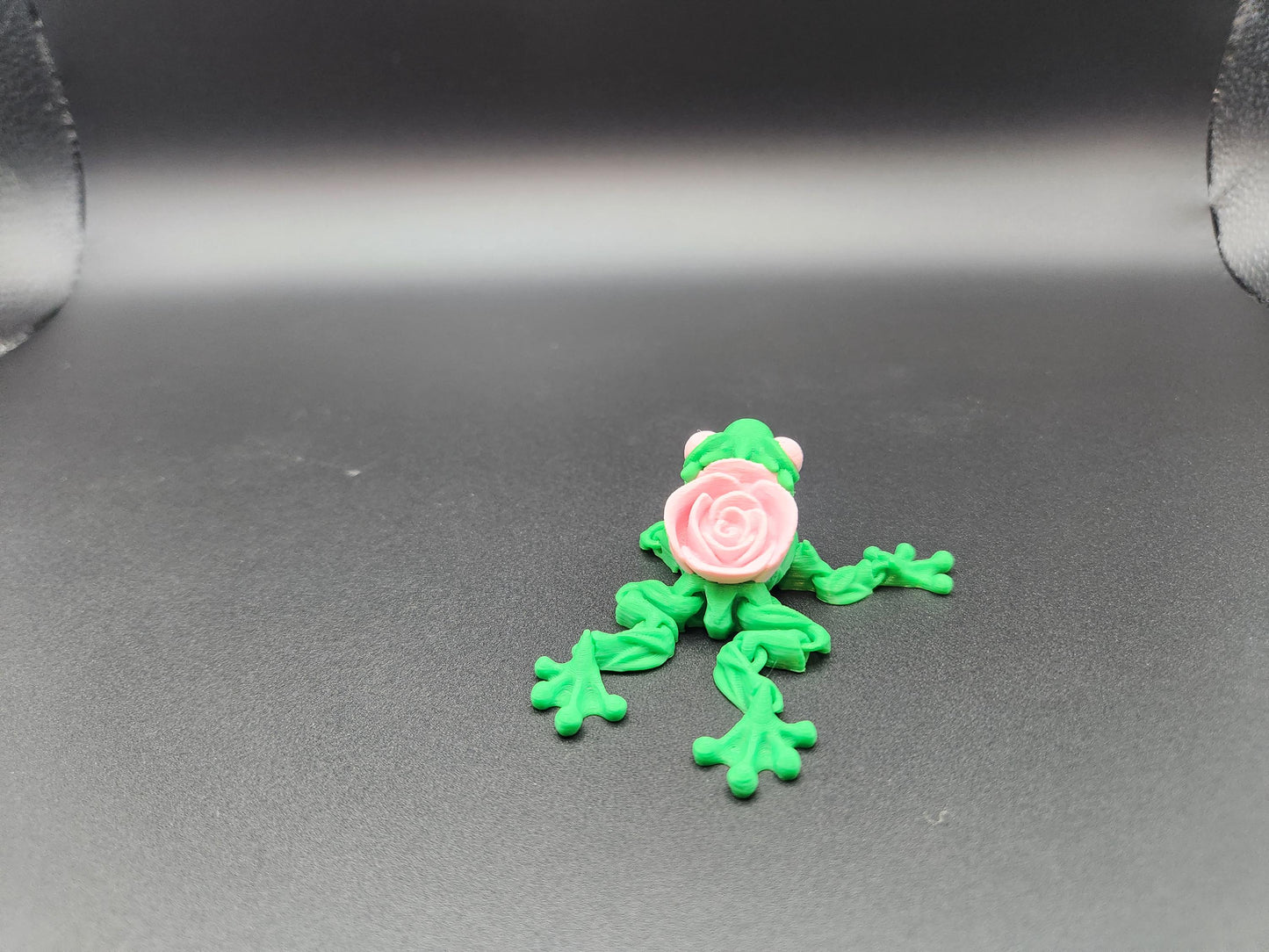 Green 3D printed articulated rose frog with a detailed pink rose on its back on a dark surface
