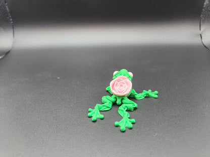 Green 3D printed articulated rose frog with a detailed pink rose on its back on a dark surface