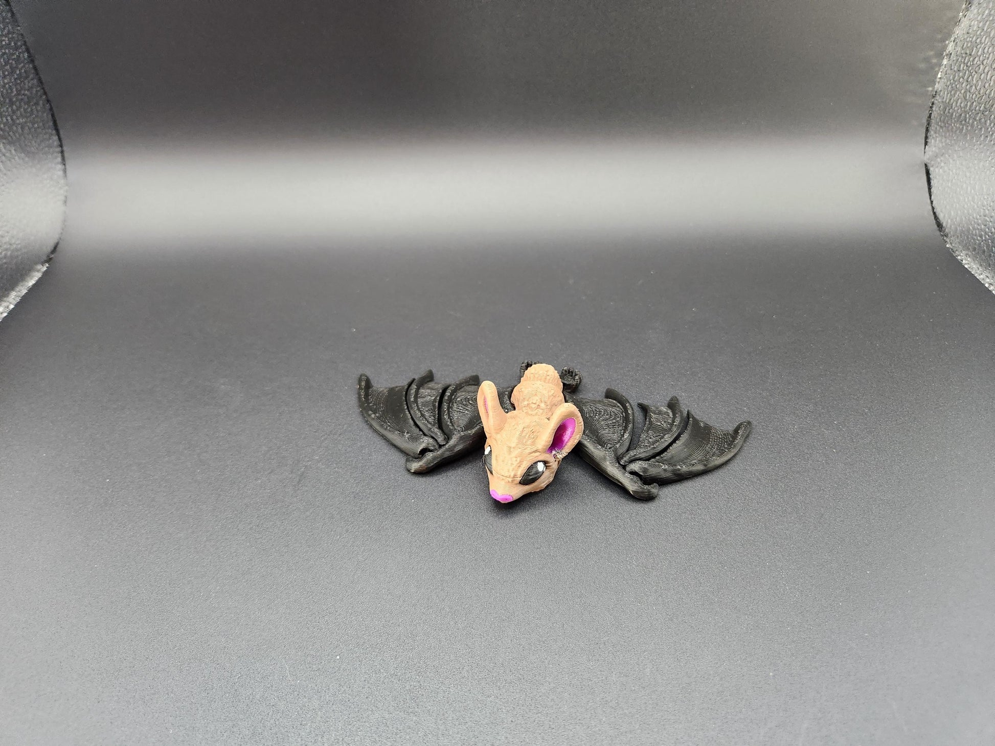 Small 3D printed bat figurine with tan head and black wings displayed on gray background