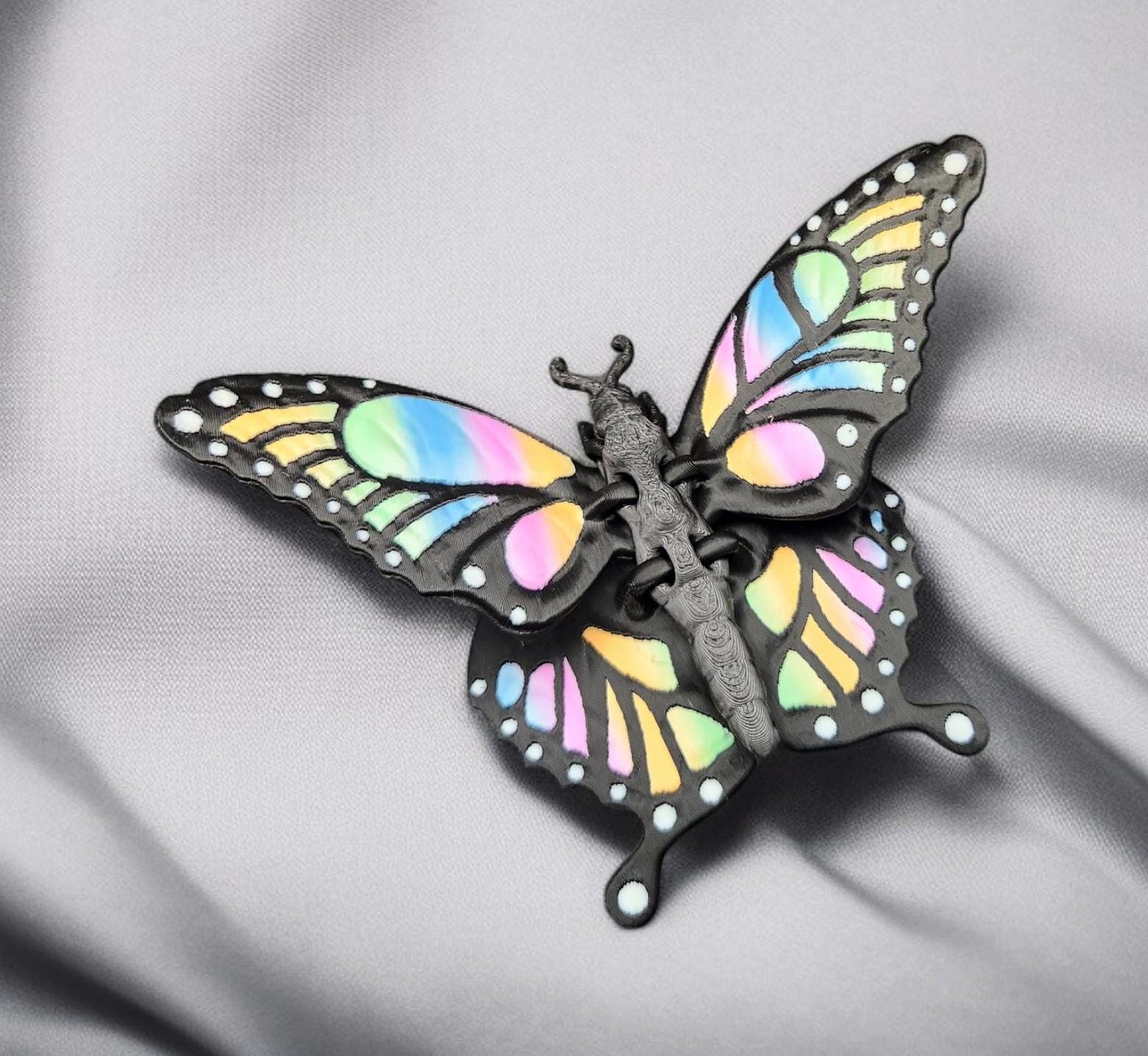 Colorful 3D printed butterfly figurine with pastel rainbow wings on a gray fabric background