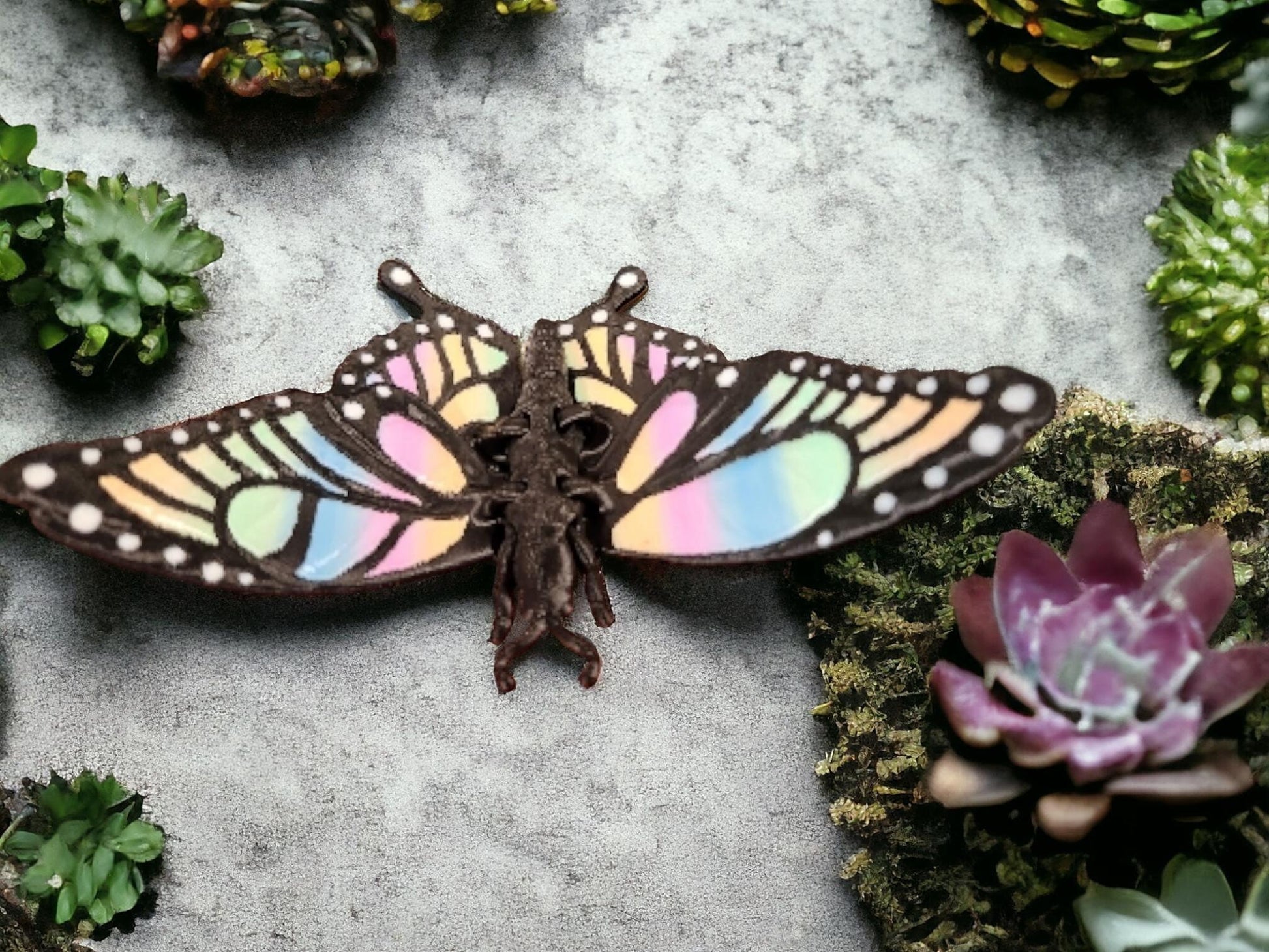 Colorful 3D printed butterfly figurine with pastel wings placed among green succulents
