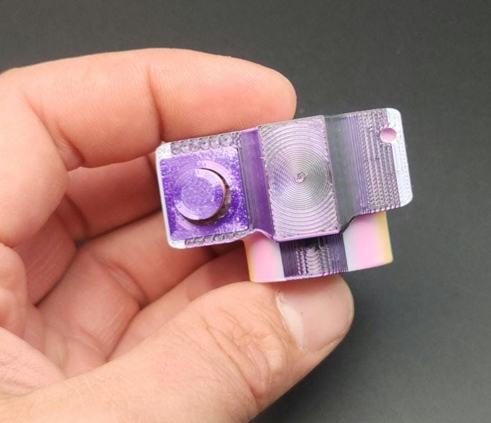 Hand holding a purple 3D printed camera fidget keychain with detailed texture and keyring hole