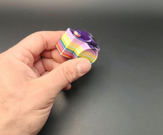 Hand holding a colorful 3D printed camera fidget keychain with a rainbow pattern and purple details