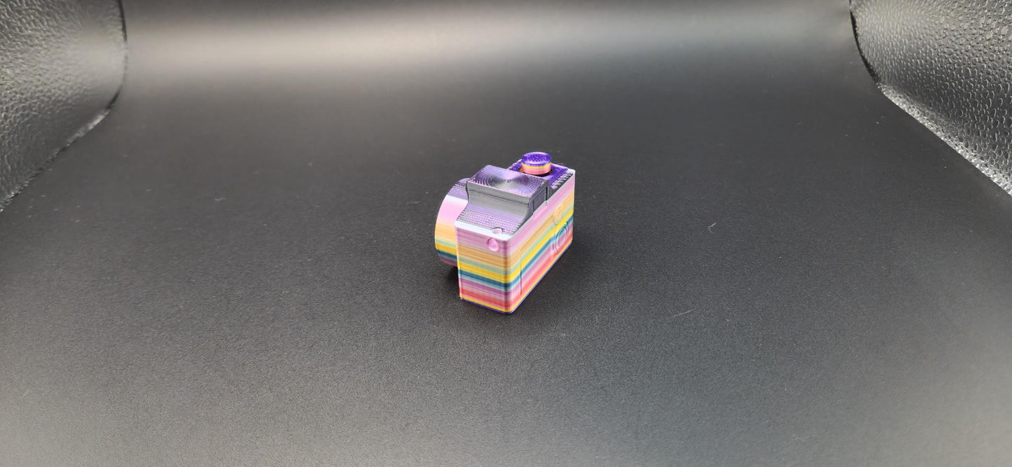 Colorful 3D printed camera fidget keychain with layered rainbow design on black background