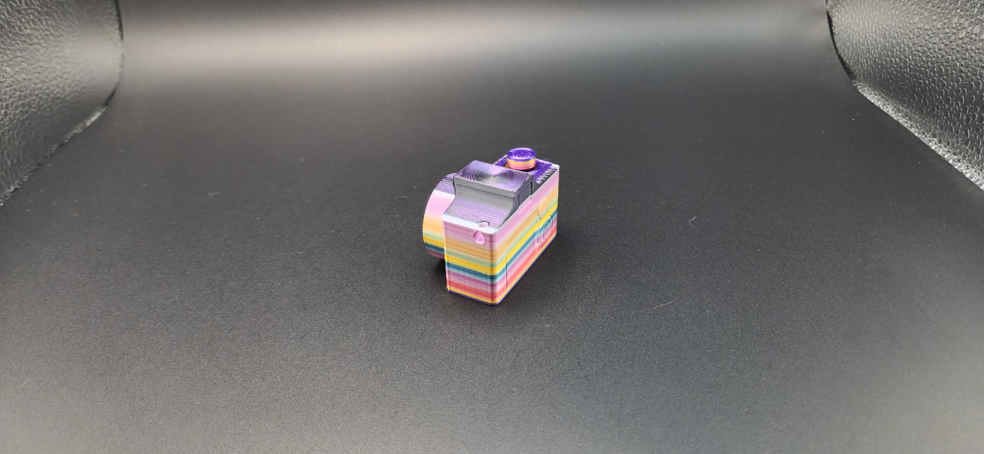 Colorful 3D printed camera fidget keychain with layered rainbow design on black background