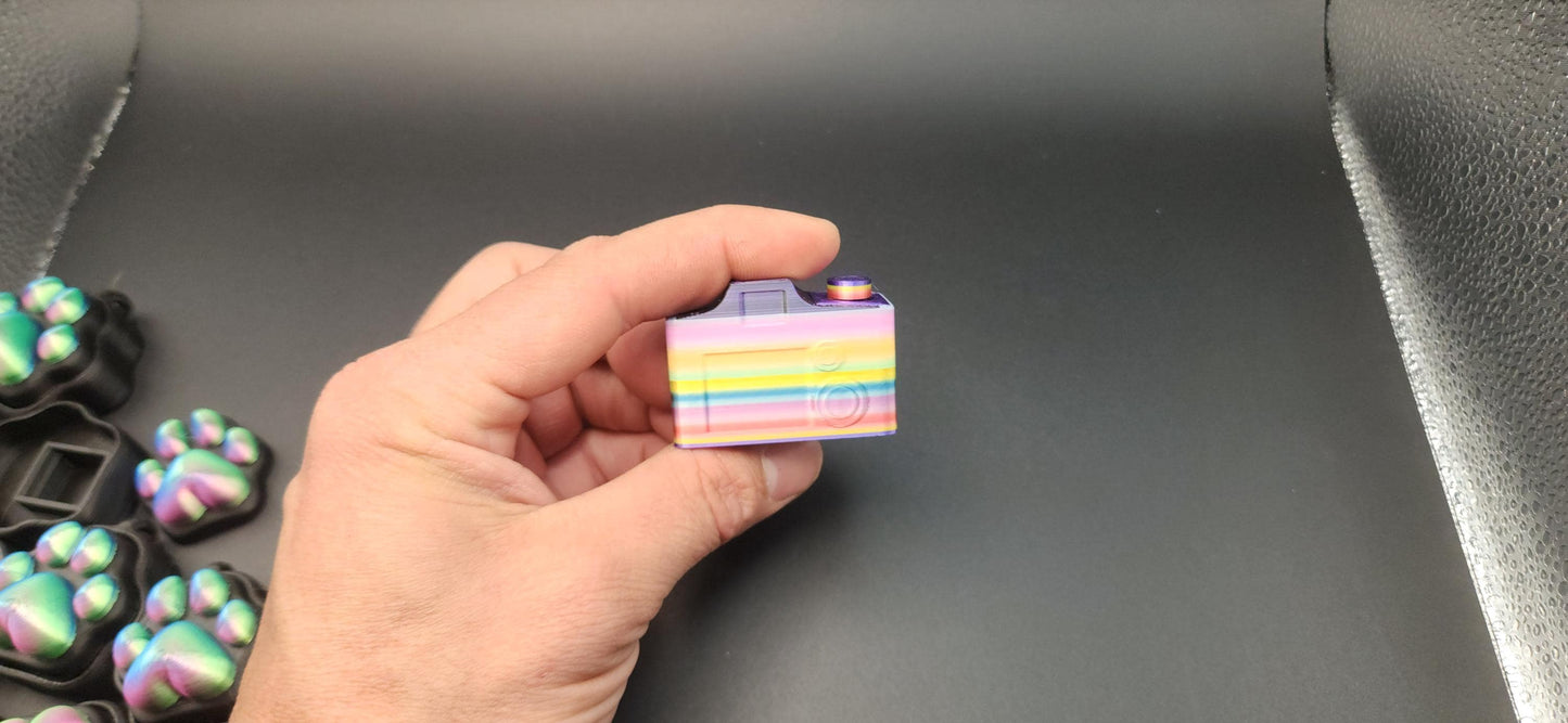 Hand holding a colorful 3D printed camera fidget keychain with a smooth black background
