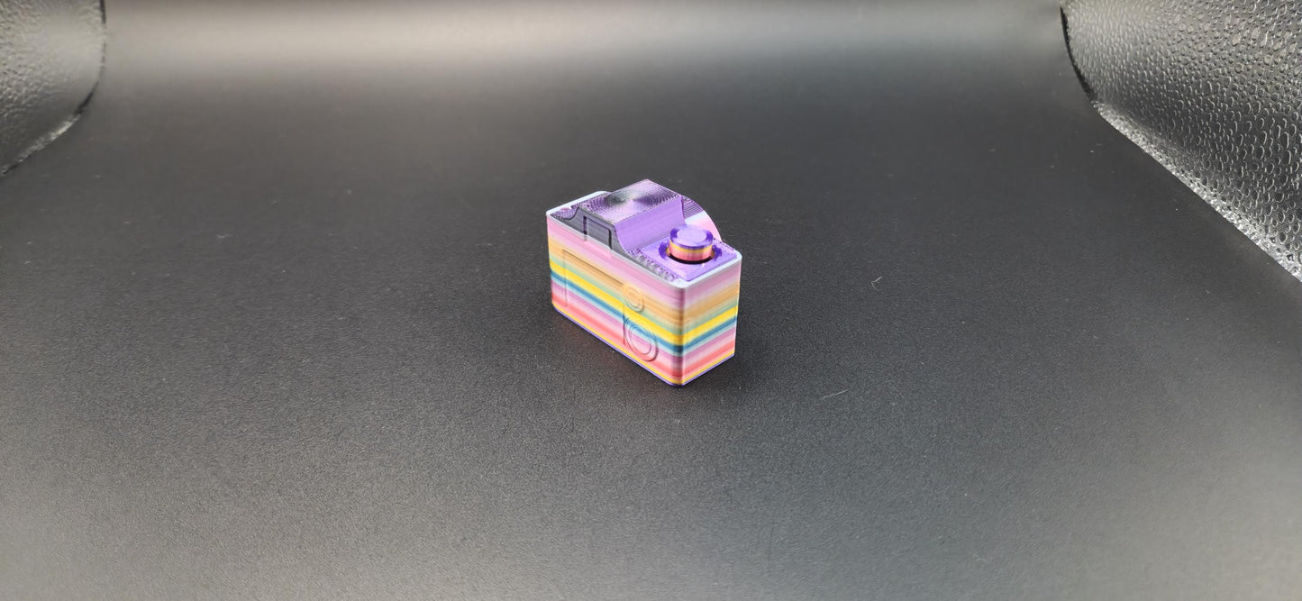 Colorful 3D printed camera fidget keychain with rainbow layers on a black background