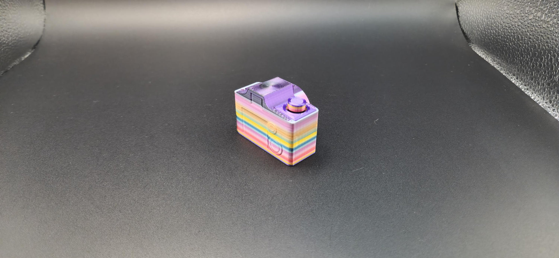 Colorful 3D printed camera fidget keychain with rainbow layers on a black background