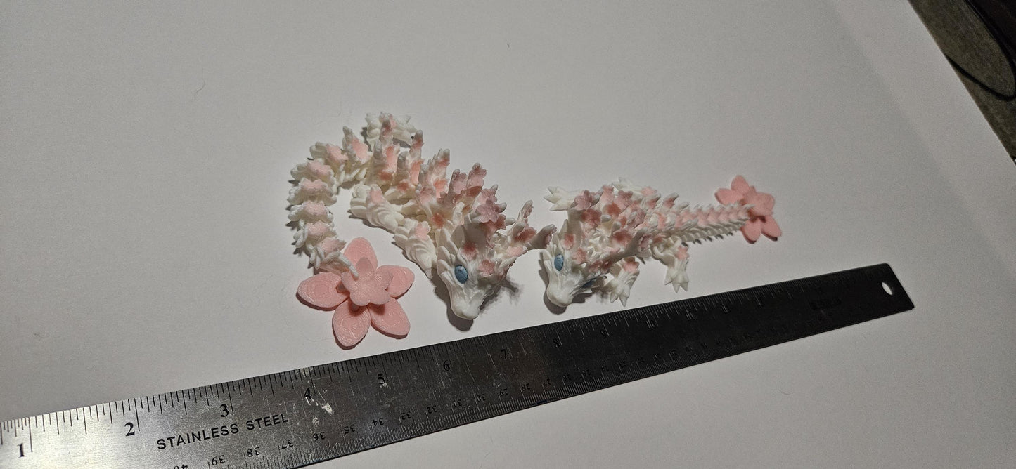 Two small 3D printed cherry blossom baby dragons with pink flowers next to a ruler for size reference