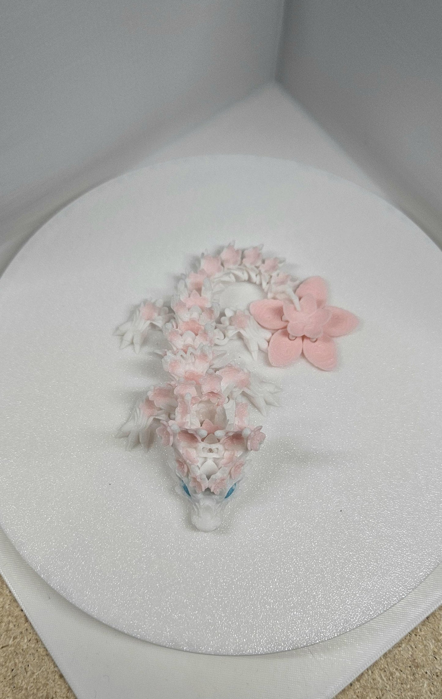 3D printed cherry blossom baby dragon in white and pink with detailed floral design on a round white surface