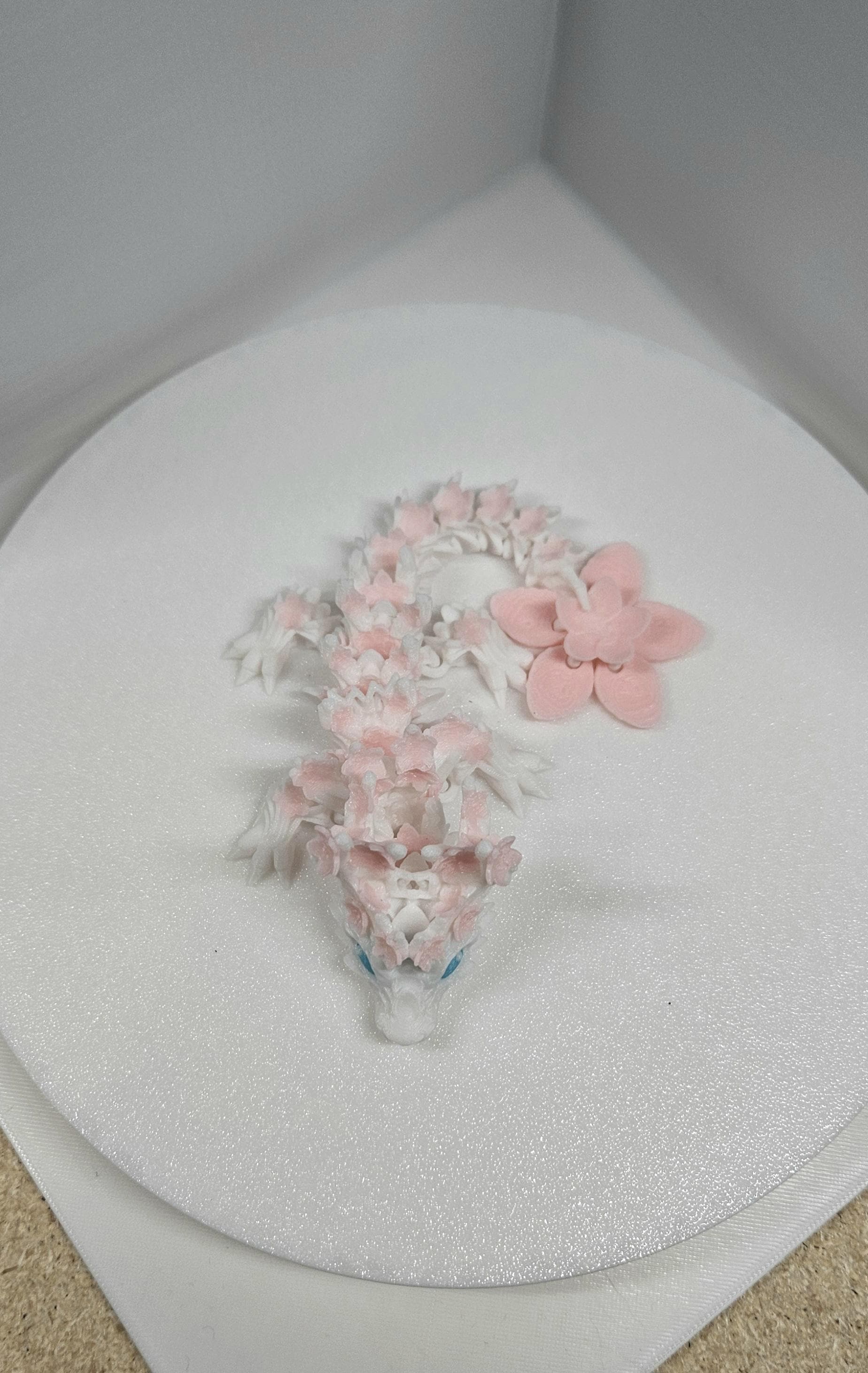3D printed cherry blossom baby dragon in white and pink with detailed floral design on a round white surface