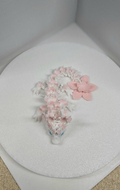 3D printed cherry blossom baby dragon in white and pink with detailed floral design on a round white surface