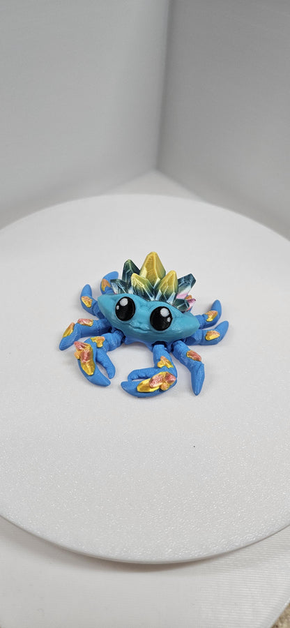 Blue 3D printed crystal crab with gold accents and large black eyes on white background