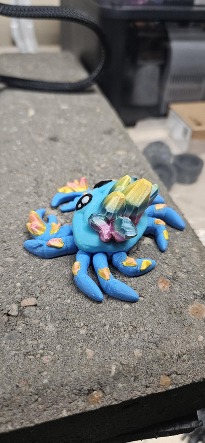 Blue 3D printed crystal crab figurine with colorful crystals on its back displayed on a concrete surface