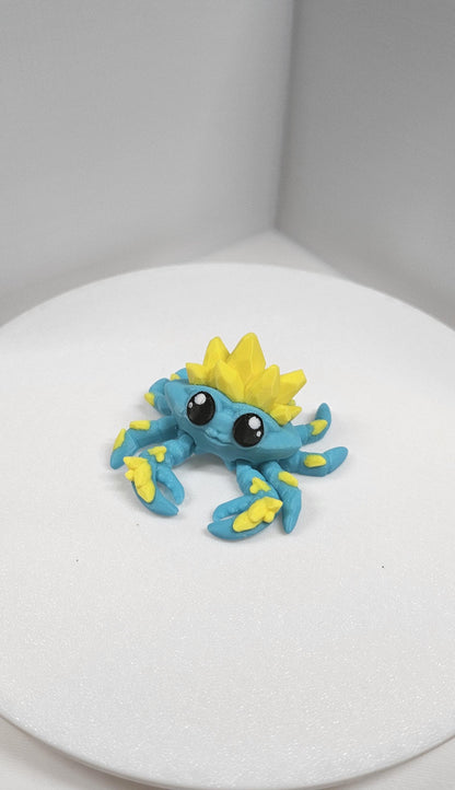 Colorful blue and yellow 3D printed crystal crab figurine with cute large eyes on white background