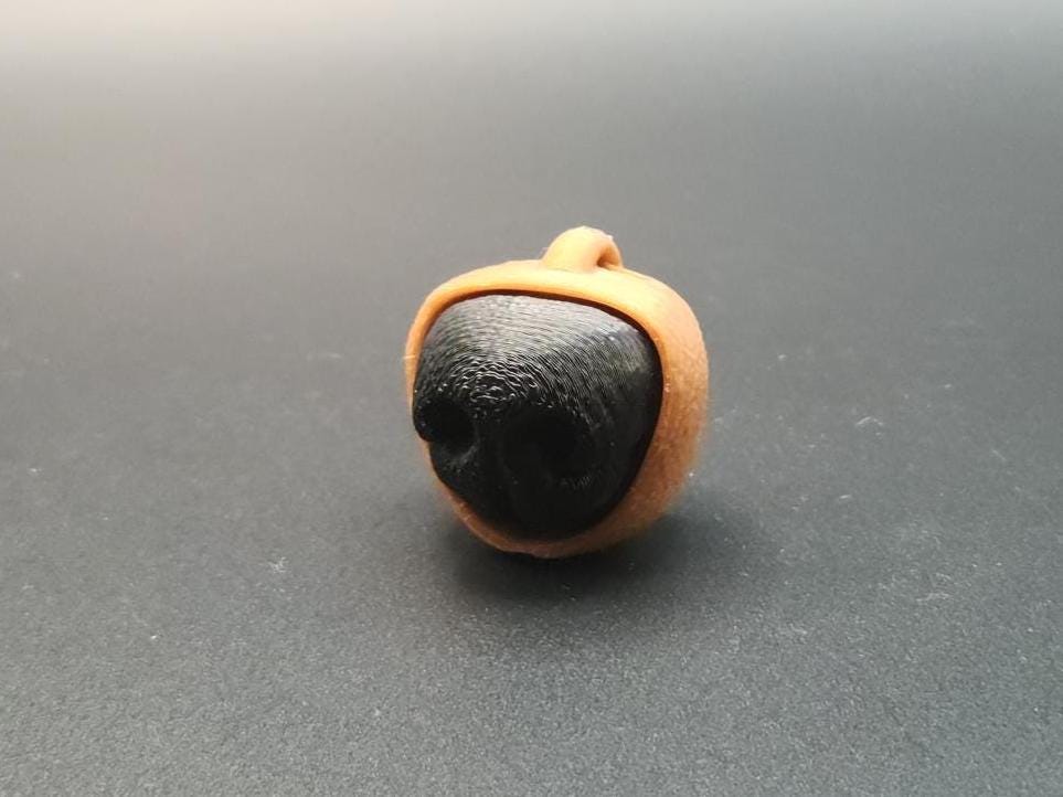 3D printed dog nose clicker keychain in black and tan colors with textured surface
