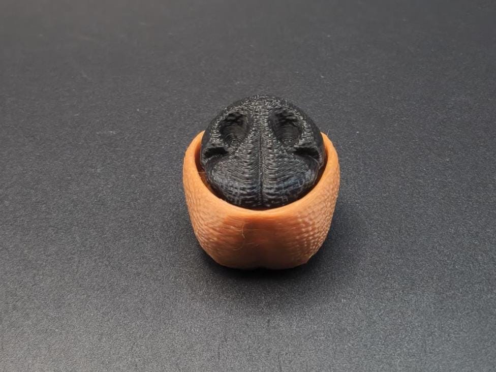 3D printed dog nose clicker keychain in black and brown details on a dark surface