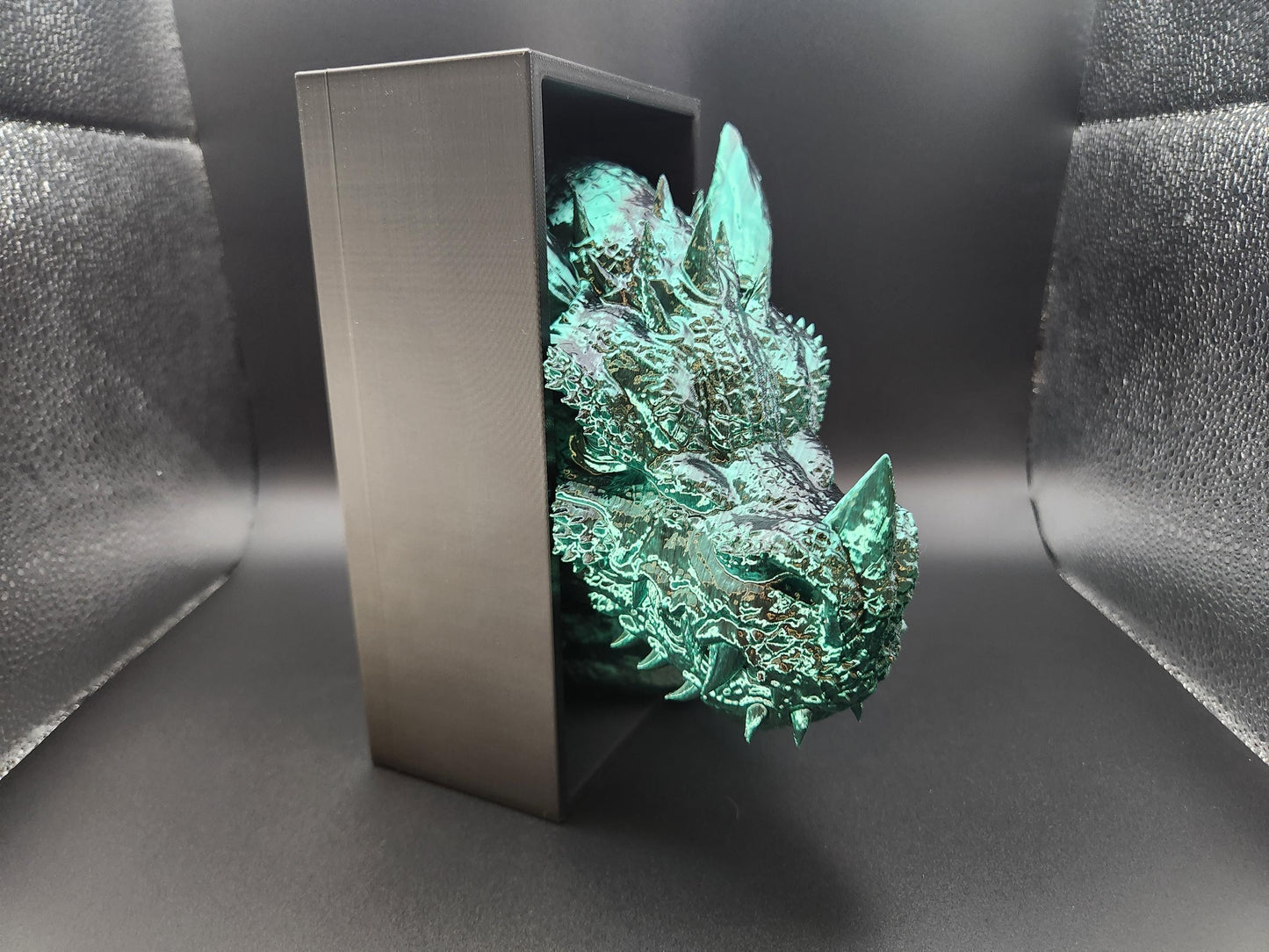 Metallic green 3D printed dragon bookend with detailed scales and spikes holding black metal bookend frame