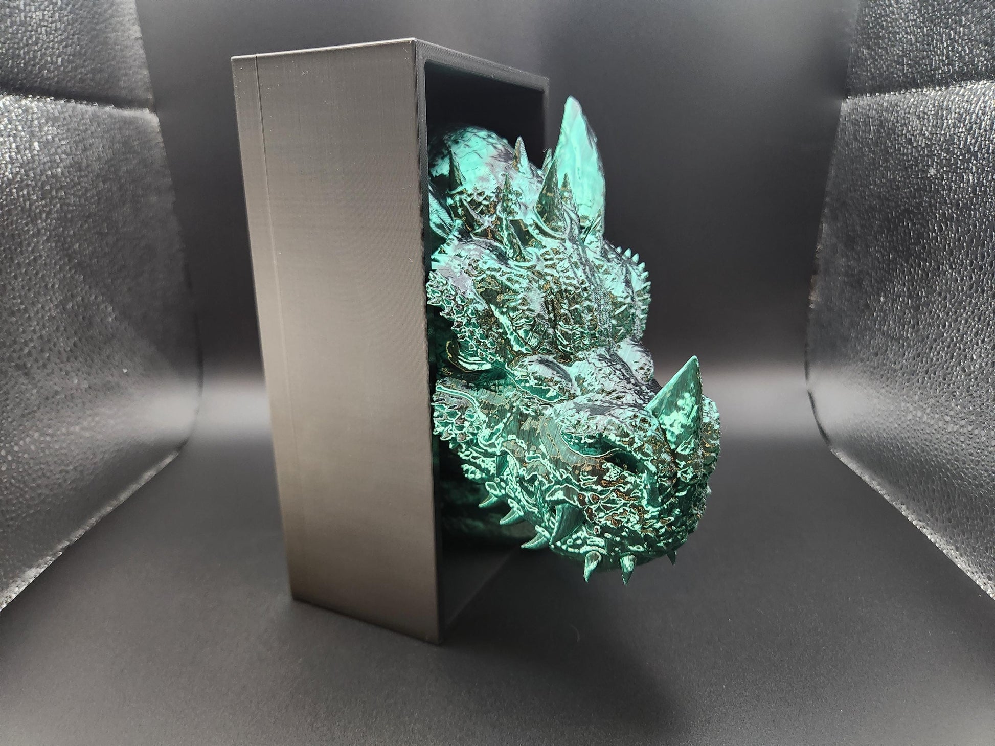 Metallic green 3D printed dragon bookend with detailed scales and spikes holding black metal bookend frame