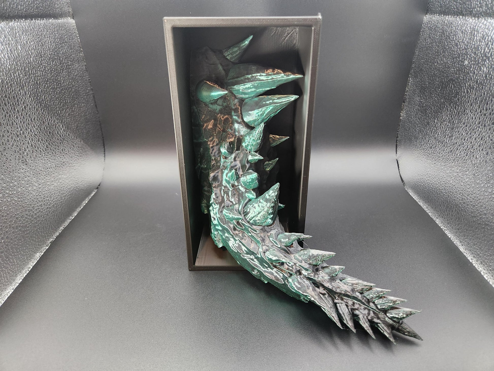 Green and black 3D printed dragon bookend with detailed scales and spikes inside a black display box