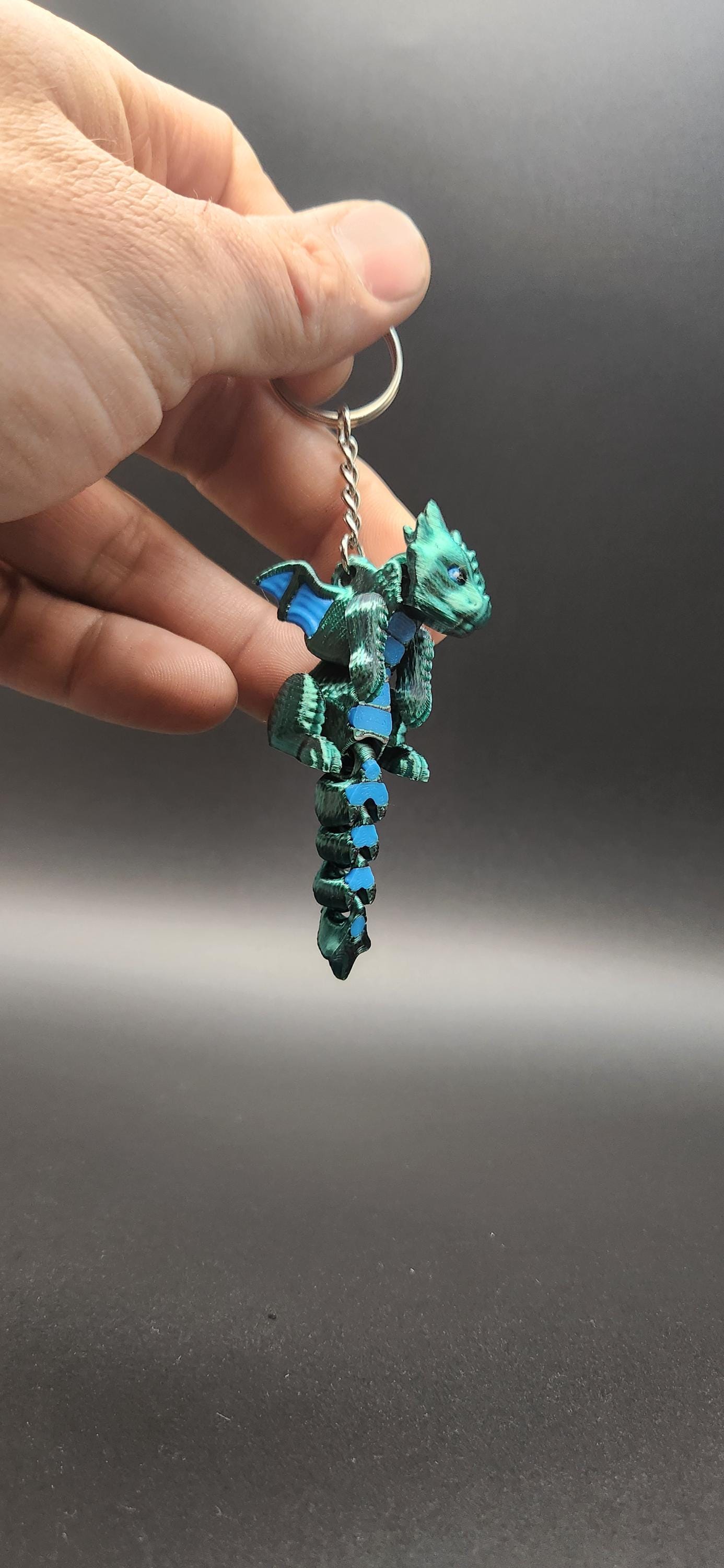 Hand holding a blue and green 3D printed dragon keychain with detailed wings and tail