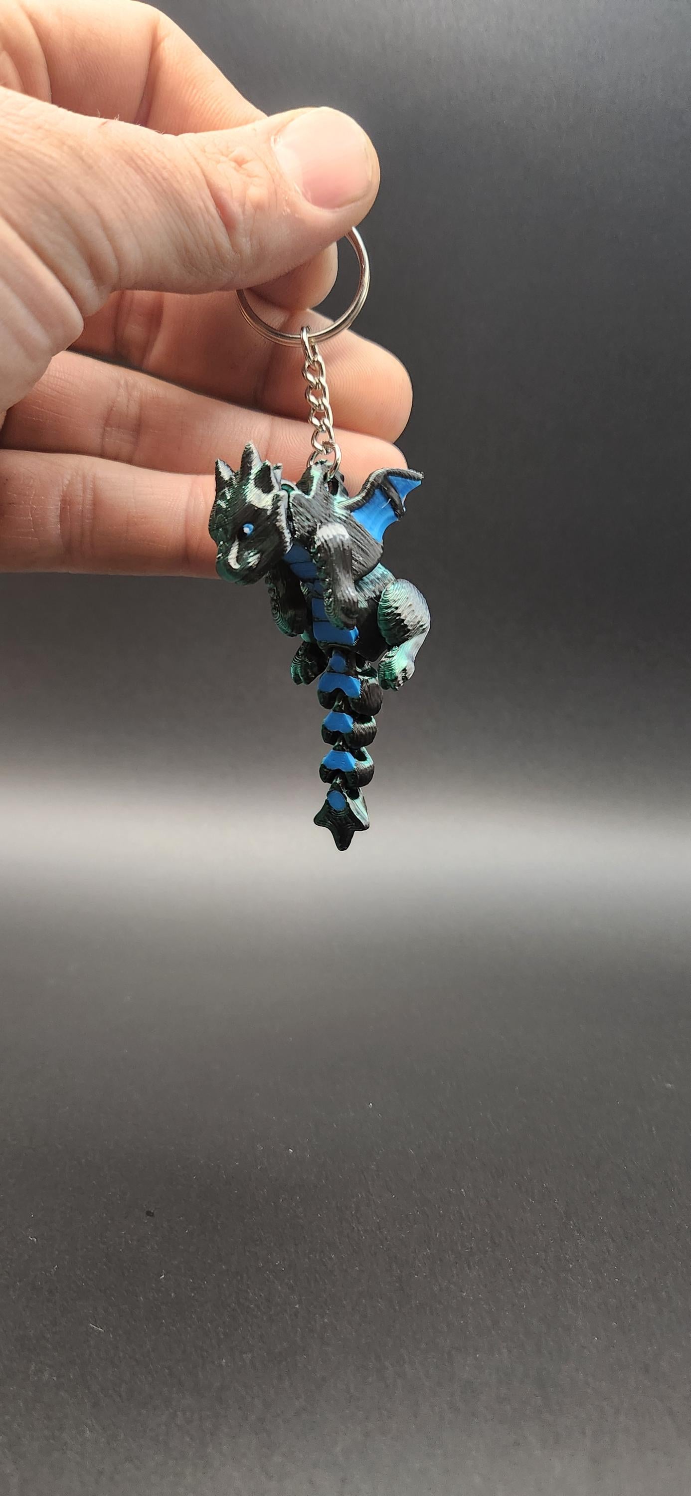 Hand holding a detailed black and blue 3D printed dragon keychain with a metal ring