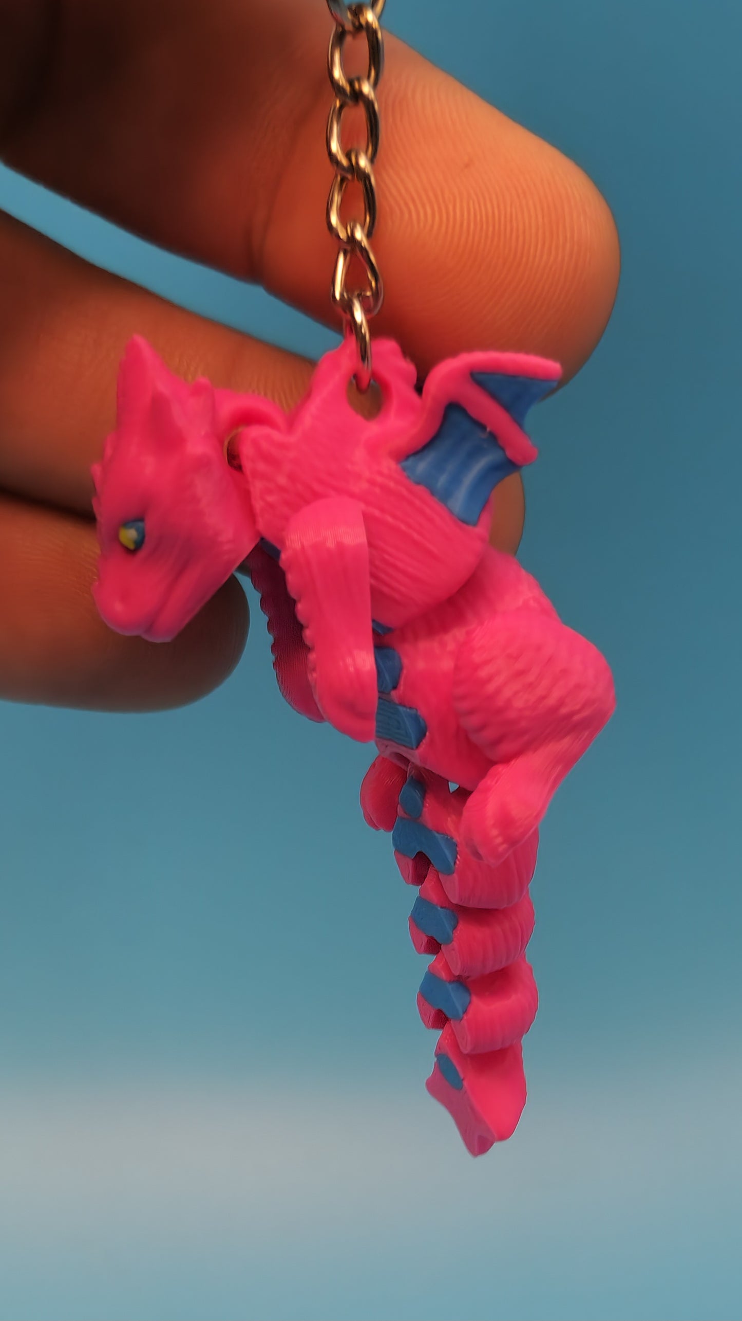 Pink and blue 3D printed dragon keychain held between fingers with detailed scales and wings