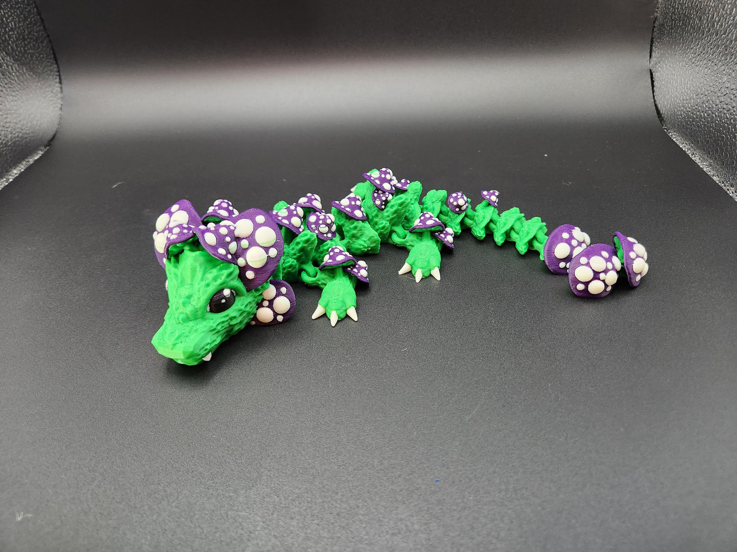 3D printed dragon mushroom toy in green with purple and white mushroom details laying on black background