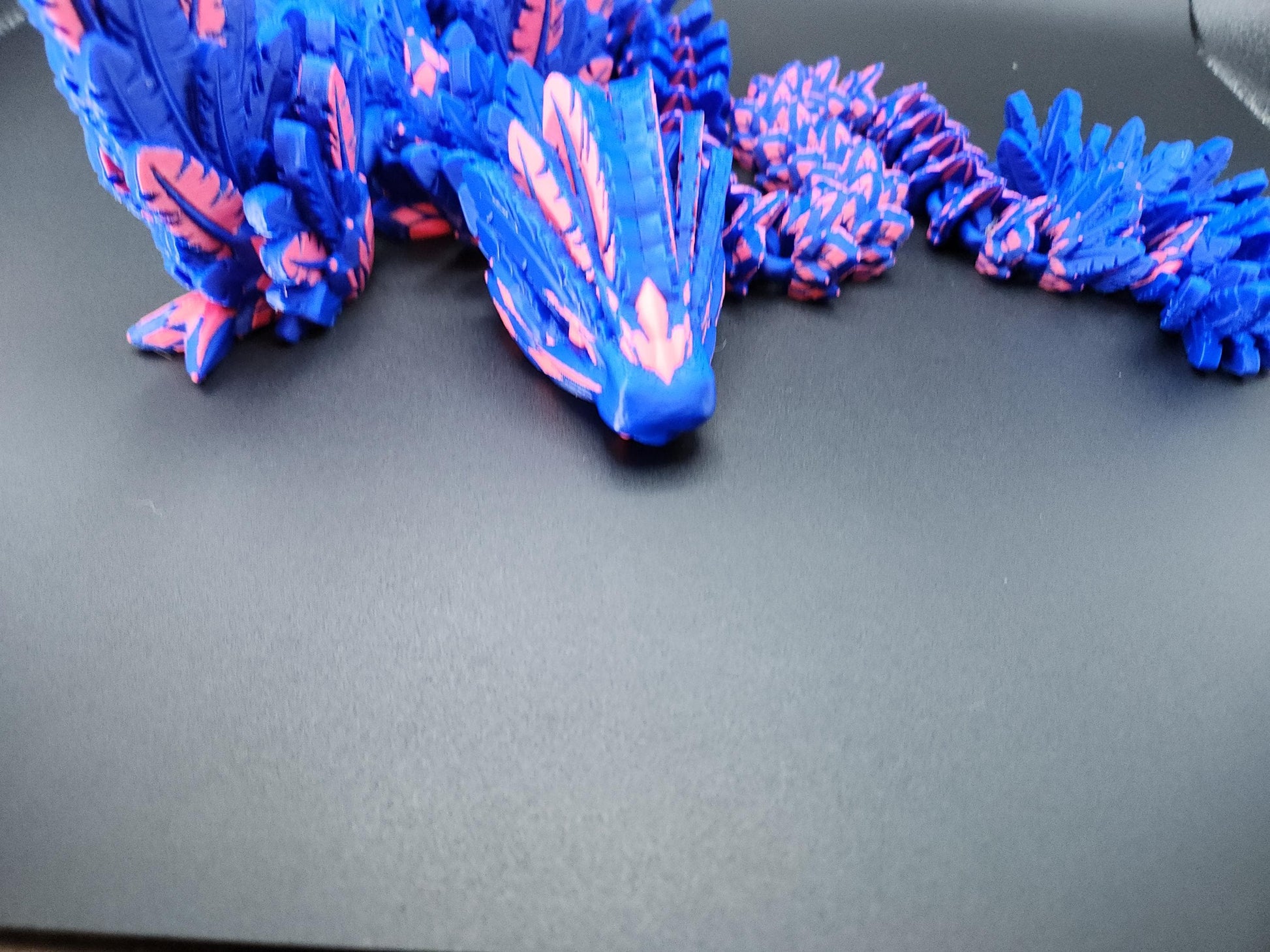 Blue and pink 3D printed feather dragon figurine with detailed feather texture on a dark surface