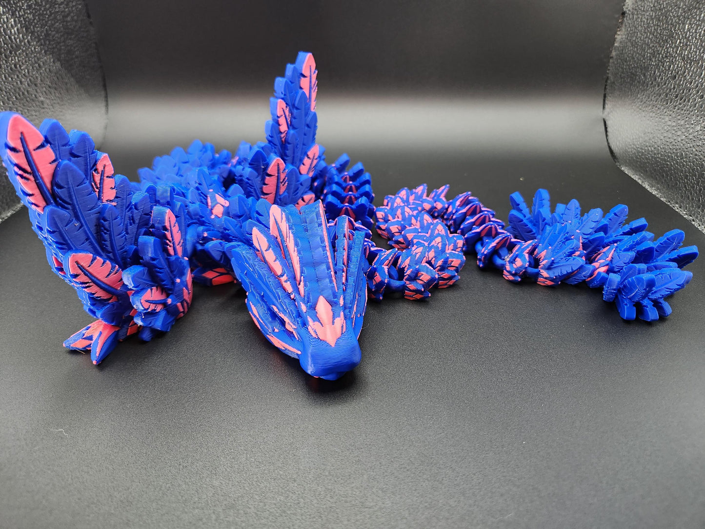 Blue and pink 3D printed feather dragon figurine with intricate feather details on black background