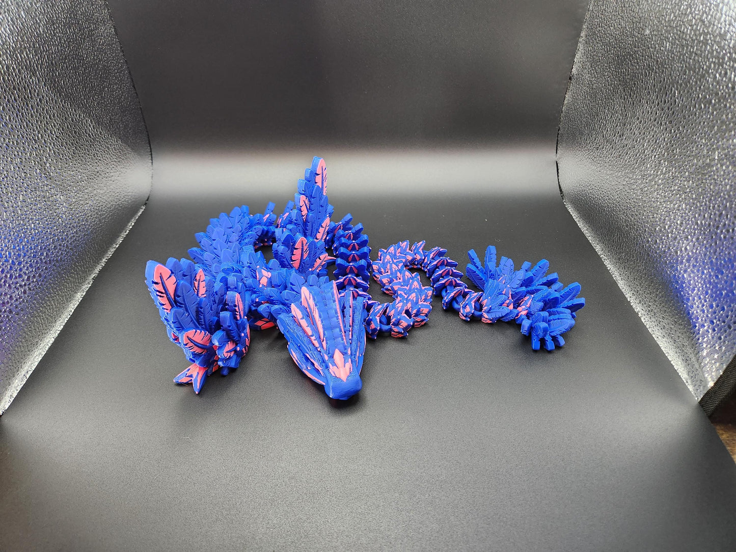 Blue and pink 3D printed feather dragon figurine with detailed wings and tail on black background