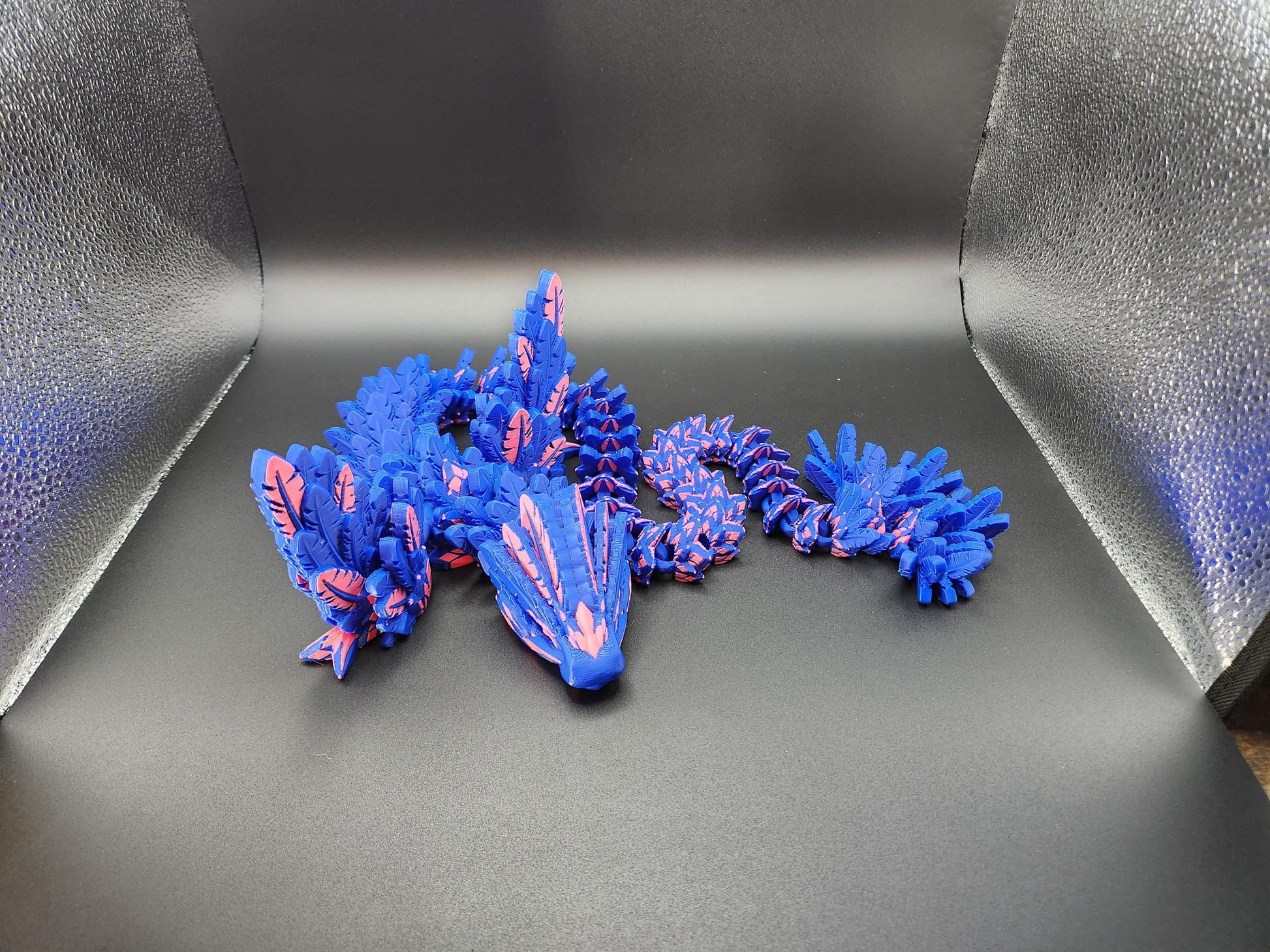 Blue and pink 3D printed feather dragon figurine with detailed wings and tail on black background