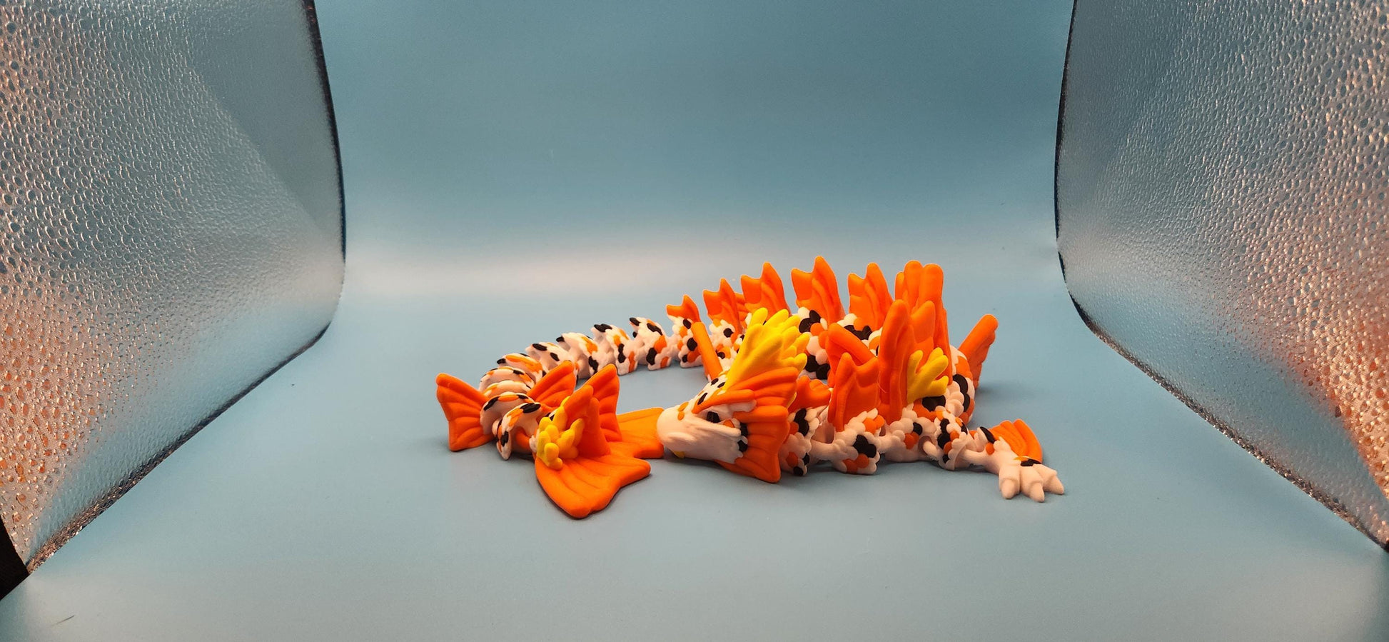 3D printed koi dragon toy in bright orange and white colors displayed on a light blue background