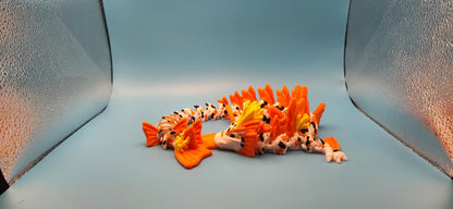 3D printed koi dragon toy in bright orange and white colors displayed on a light blue background