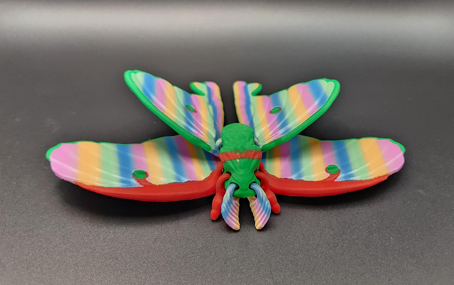 Colorful 3D printed luminous moth with rainbow-striped wings displayed on black background