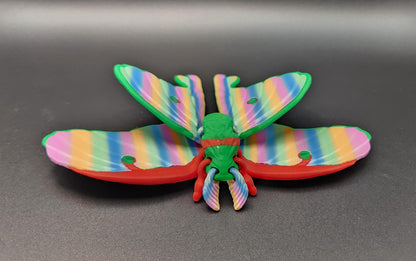 Colorful 3D printed luminous moth with rainbow-striped wings displayed on black background