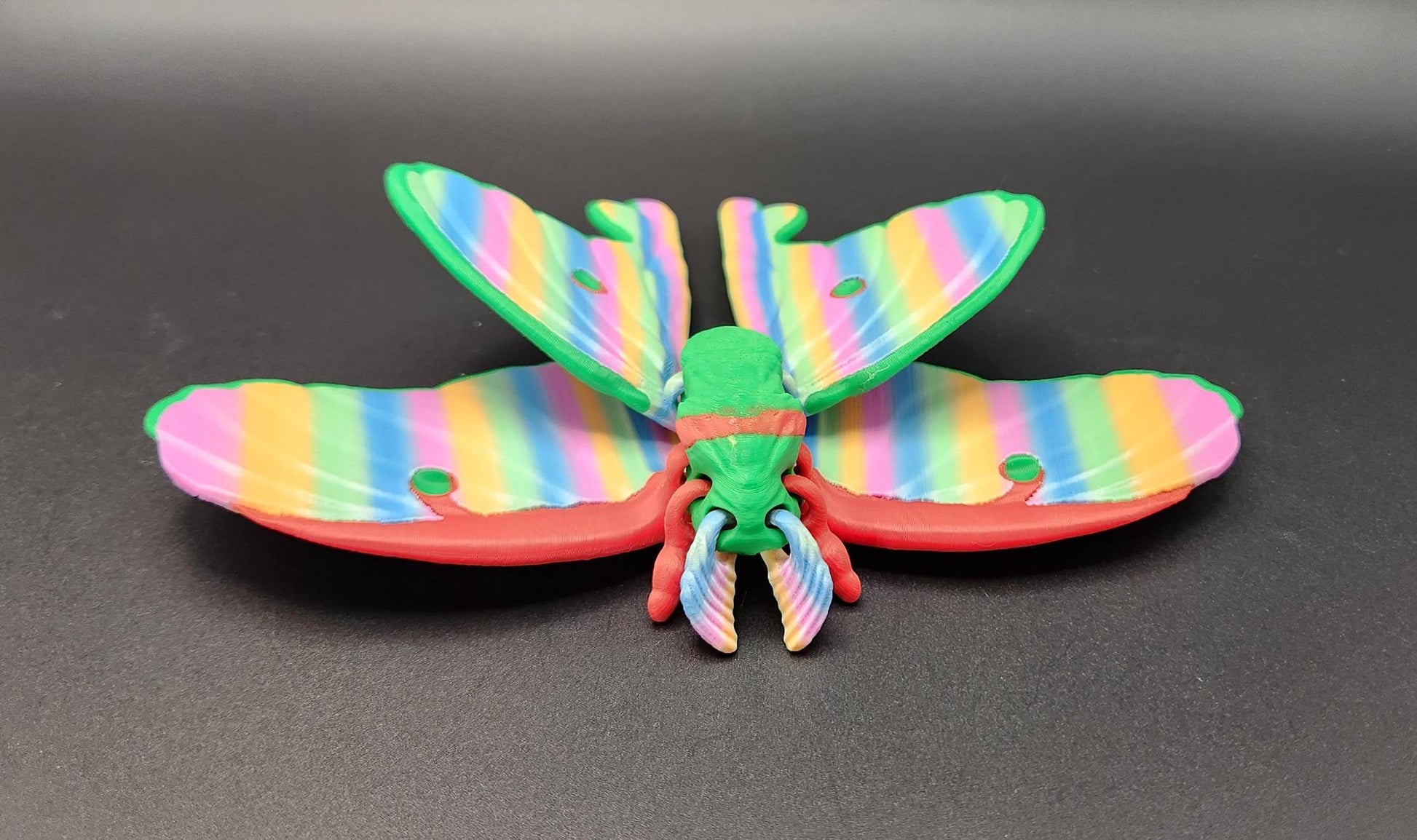 Colorful 3D printed luminous moth with rainbow striped wings on a black background