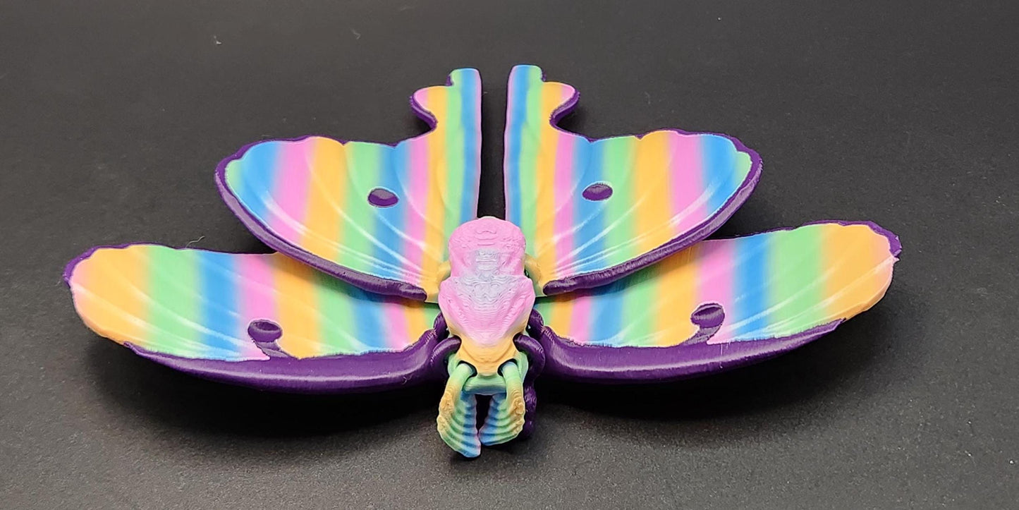Colorful 3D printed luminous moth with rainbow stripes displayed on a dark background