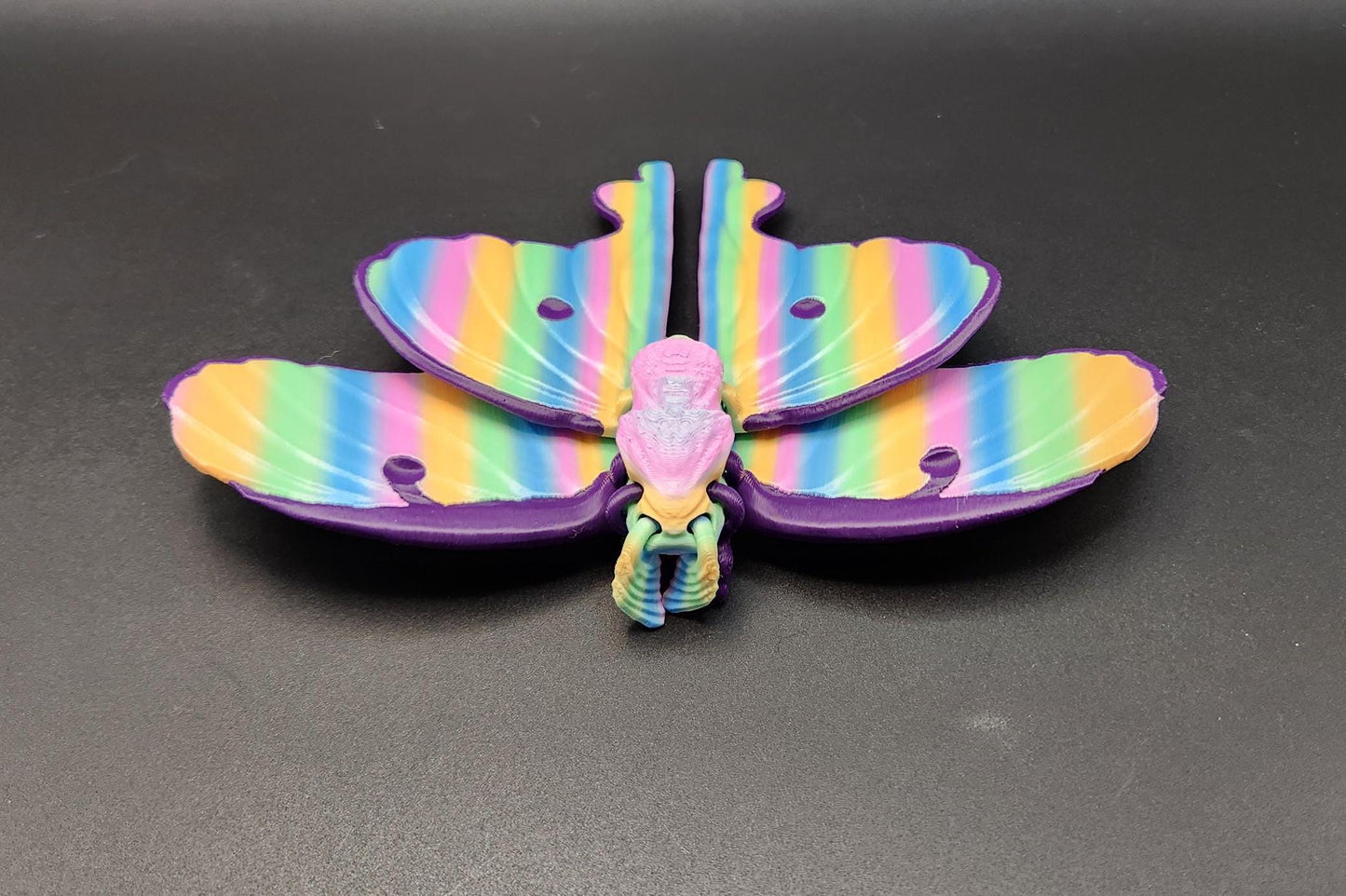 Colorful 3D printed luminous moth with rainbow striped wings displayed on black surface