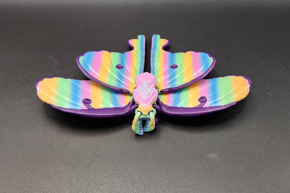 Colorful 3D printed luminous moth with rainbow striped wings displayed on black surface